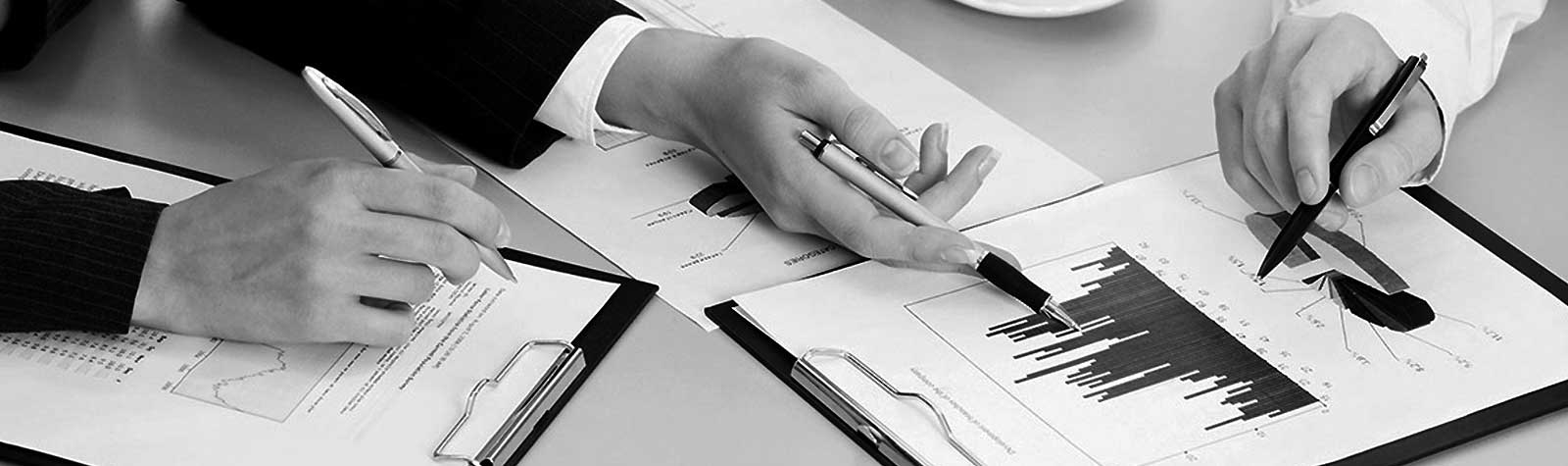 Tres manos con bolígrafos ante unos documentos relativos a gráficas. Foto en blanco y negro.