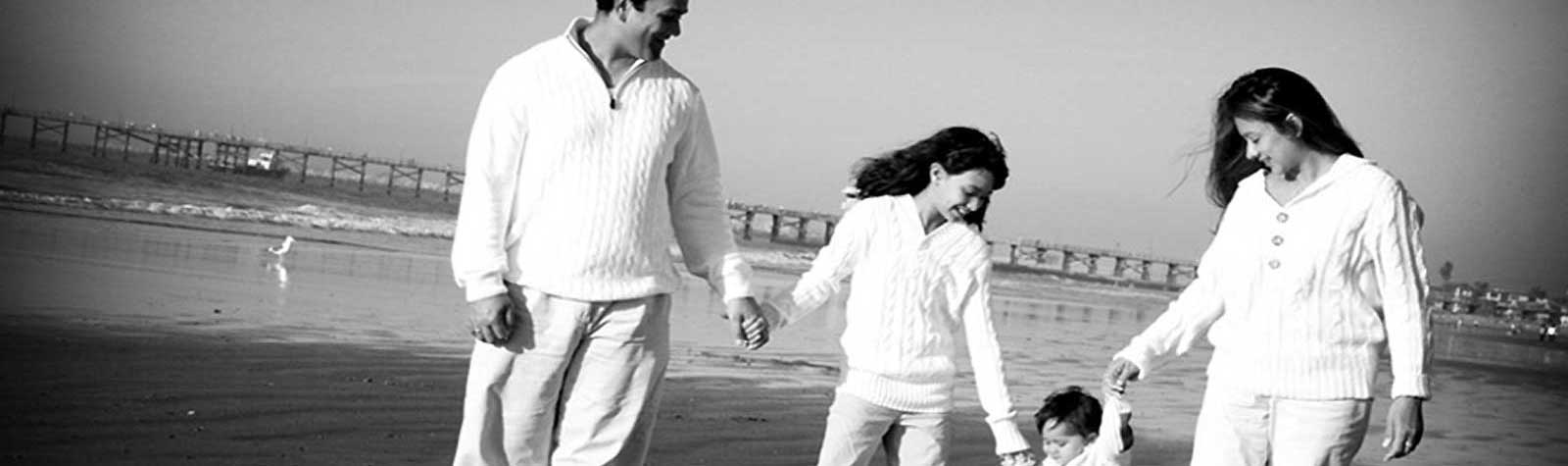 Familia de una pareja hombre-mujer con dos niñas pequeñas paseando por la playa. Foto en blanco y negro.